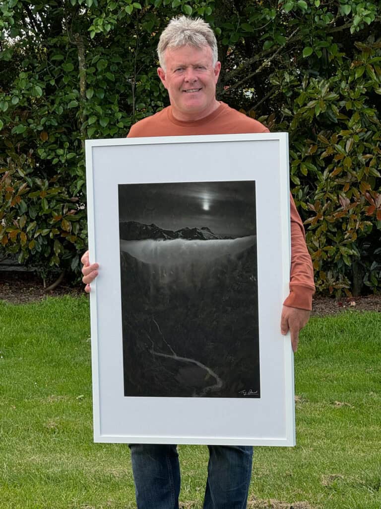 Professional photographer Tony Stewart holds framed artwork.