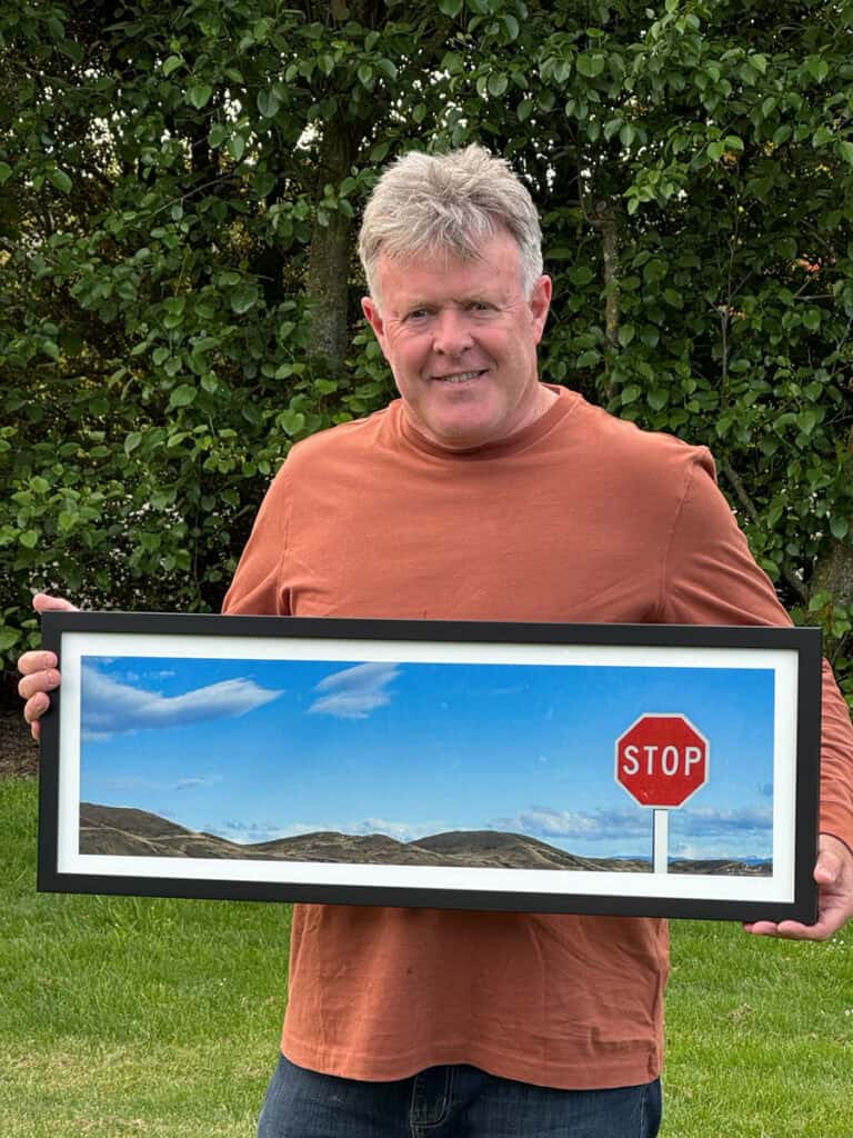 Professional photographer Tony Stewart holds framed photo artwork.