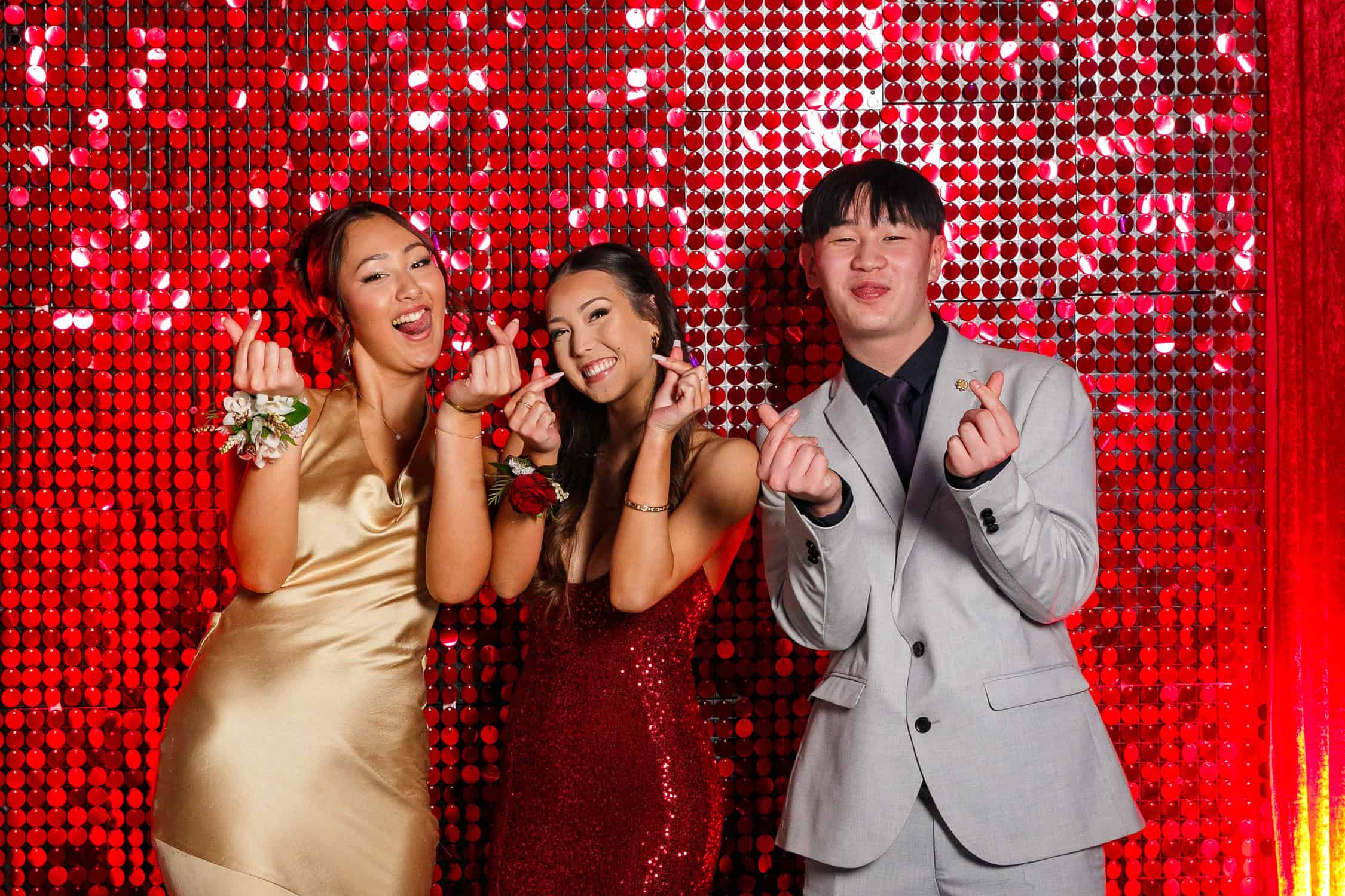 Three high school students pose for photos against sparkly red background at their school ball.