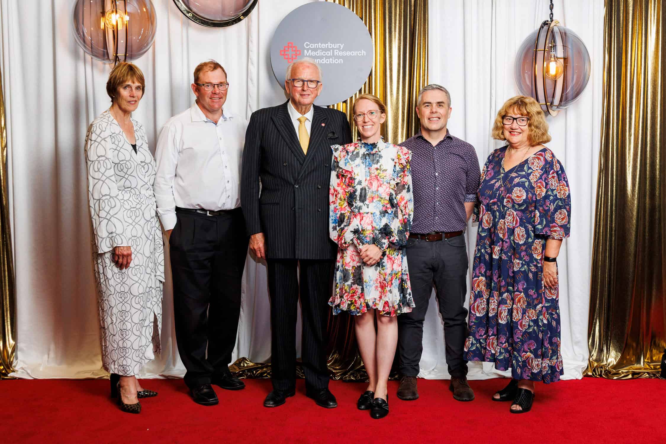 Benefactors and recipients pose by media wall during a fundraising event.