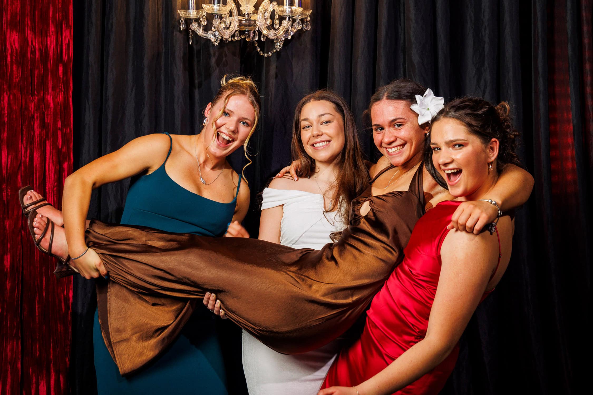 Girls hold each other while posing at a photo booth at their school ball.